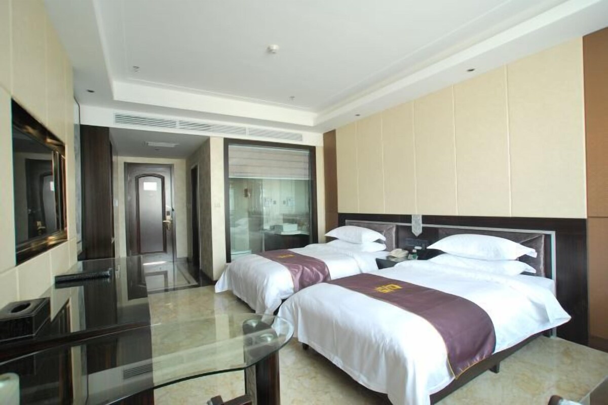 A hotel room with two beds, a glass table, a mirror, and a view of the hallway.