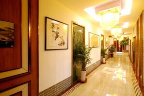 Un couloir d’hôtel décoré avec des œuvres d’art encadrées, des plantes en pot et un sol à motifs.