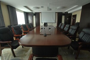 Una sala de conferencias con una larga mesa, varias sillas, una pantalla de proyector y una pizarra.
