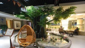 A tranquil indoor garden with a large artificial tree, a wicker chair, and a small pond. - Kai Bin Hotel (Baiyin)