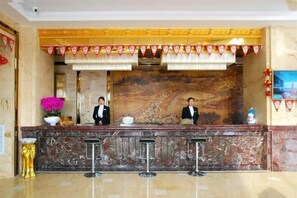 A hotel reception area with a marble counter, two receptionists, a decorative wall, and a small plant. - Kai Bin Hotel (Baiyin)