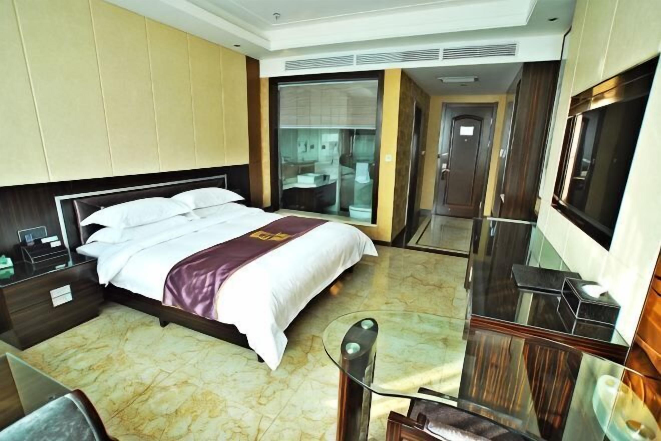 Une chambre d’hôtel comprenant un lit, un bureau, une chaise, une télévision et une salle de bain avec une porte en verre.