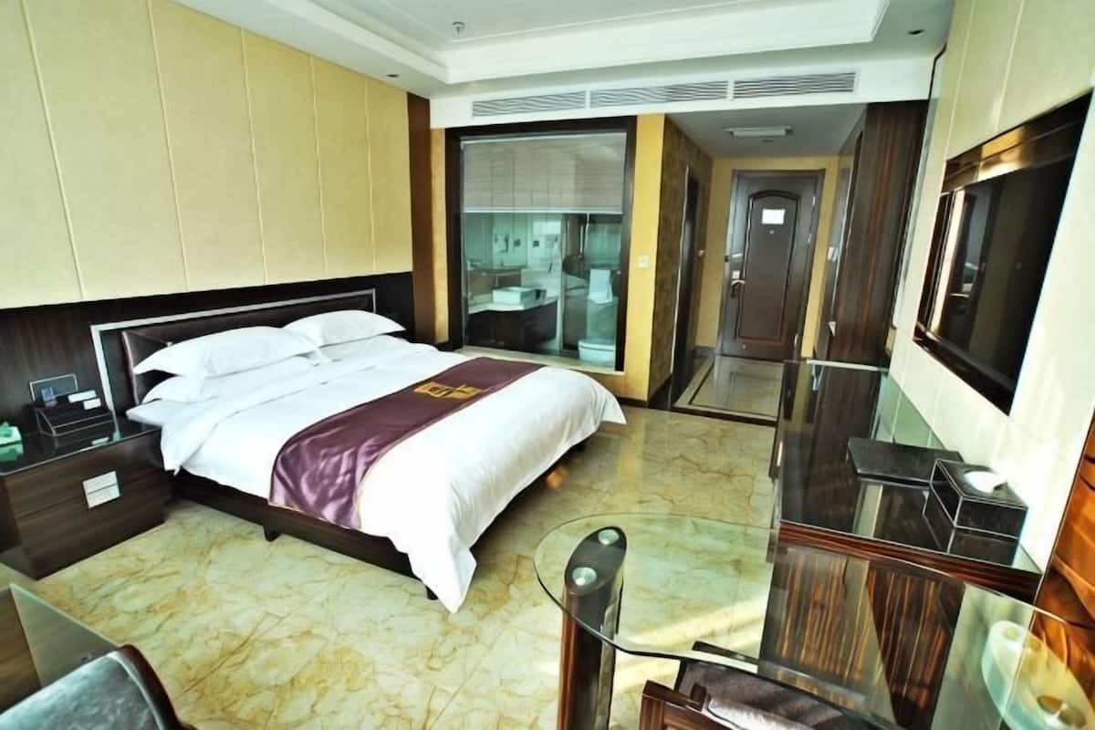 Una habitació d'hotel amb un llit, una taula de treball, una cadira, una televisió i un bany amb porta de vidre.