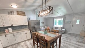 A spacious kitchen with white cabinets, a wooden dining table, and a modern chandelier. - Serene Home with PRIVATE Pool - Near Beaches - Dog Friendly - Firepit&Large Yard (Freeport)