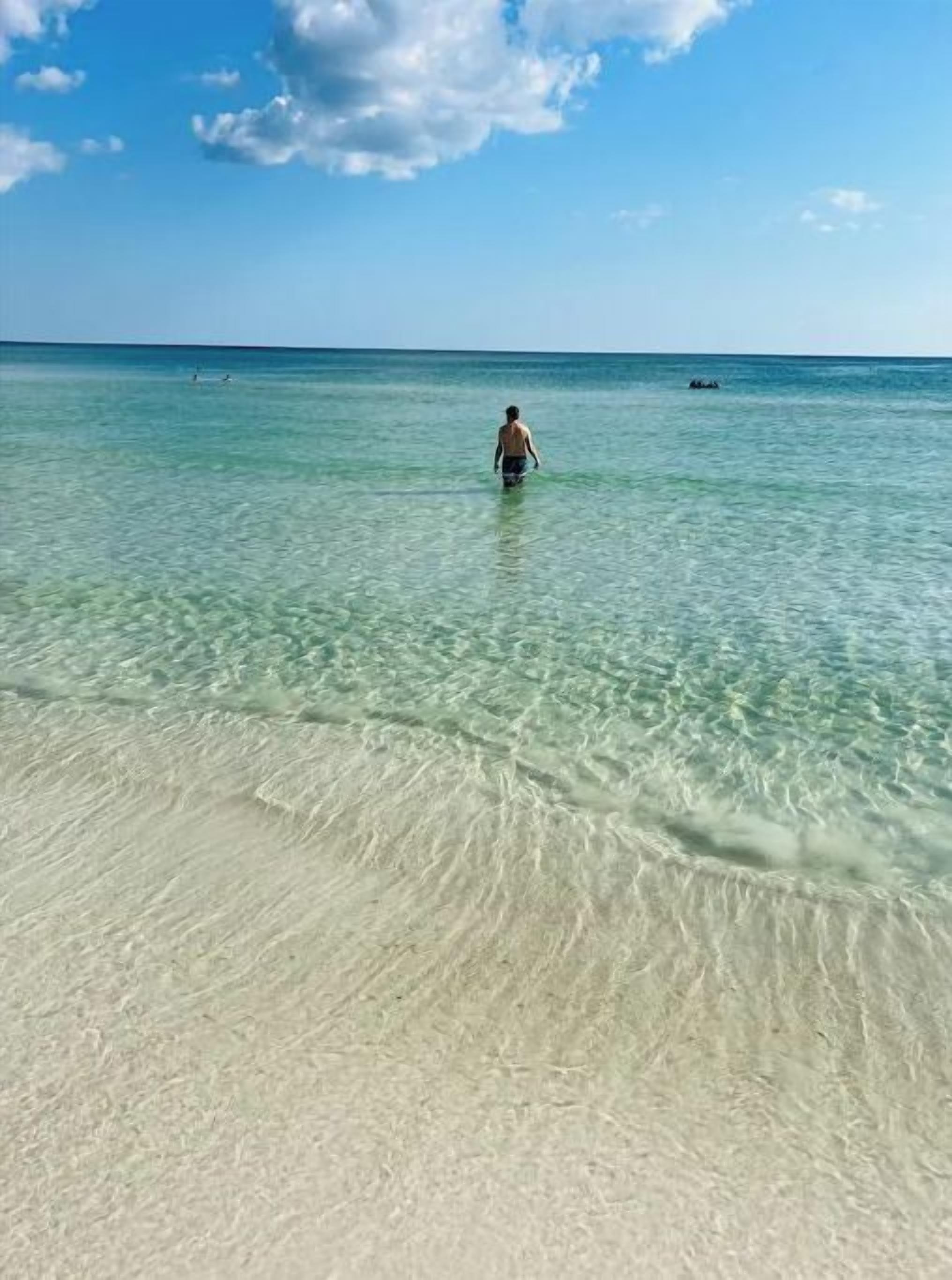 Uma praia com águas cristalinas e pouco profundas, e uma pessoa ao longe.