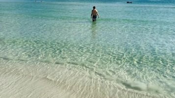 Uma praia com águas cristalinas e pouco profundas, e uma pessoa ao longe.