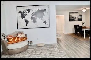 A modern living room with a world map, a dining area with a wooden table and chairs, and a cozy seating area with a cushion and a small table. - Lake house scenic view with close proximity to the beach and necessities (Jacksonville)