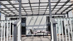 A covered outdoor seating area with a metal table and chairs, a glass door entrance, and a metal roof structure. - Lake house scenic view with close proximity to the beach and necessities (Jacksonville)