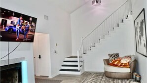 A modern living room with a flat-screen TV, a fireplace, a staircase, and a cozy seating area with cushions. - Lake house scenic view with close proximity to the beach and necessities (Jacksonville)