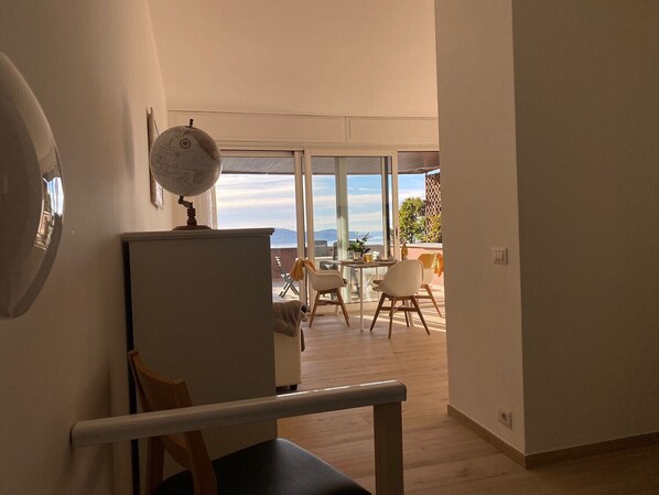 A room with a wooden floor, a white desk, a globe on a shelf, and a balcony with a view of the sea. - Barbara apartment with lake view in Ghiffa (Ghiffa)