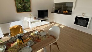 A living room with a TV, dining table, chairs, a painting, and a fireplace.