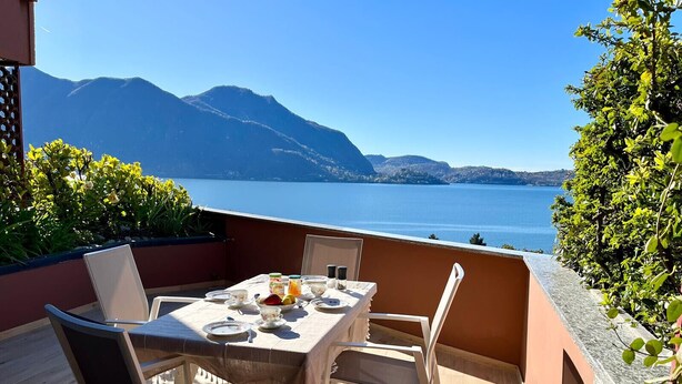 A terrace with a table set for two, overlooking a body of water and mountains.