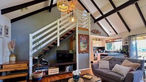 Un salón acogedor con una escalera, suelo de madera, un sofá gris, una mesa de centro y una televisión.