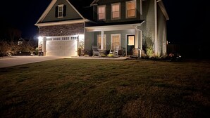 Casa de dos pisos con garaje, fachada de piedra y un porche delantero bien iluminado.