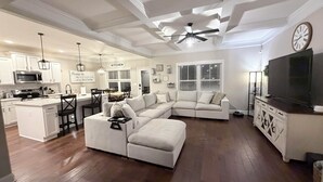 Un espacio habitable amplio con un sofá seccional en forma de L, una cocina con armarios blancos y un comedor con mesa y sillas.