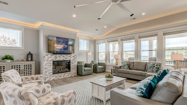 A spacious living room with a fireplace, comfortable seating, large windows, and a ceiling fan. - Happy As a Clam  | 230 ft to the beach | Private Pool, Hot Tub, Dog Friendly (Virginia Beach)