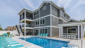 A multi-story building with a swimming pool, outdoor seating, and a bar area. - Happy As a Clam  | 230 ft to the beach | Private Pool, Hot Tub, Dog Friendly (Virginia Beach)