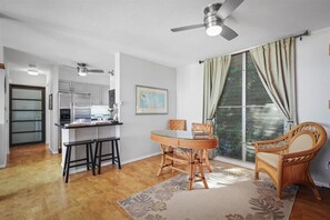 Cocina compacta con electrodomésticos modernos, comedor con mesa redonda y sillas, y un gran ventanal con cortinas.