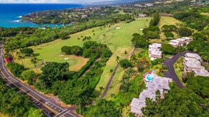 An aerial view of a golf course with a swimming pool, surrounded by lush greenery and residential buildings. - Ocean & Golf Course View Condo at Keauhou Akahi | 1 Bedroom + Murphy Bed (Kailua Kona)