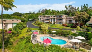 A resort with a swimming pool, outdoor seating, and lush greenery. - Ocean & Golf Course View Condo at Keauhou Akahi | 1 Bedroom + Murphy Bed (Kailua Kona)