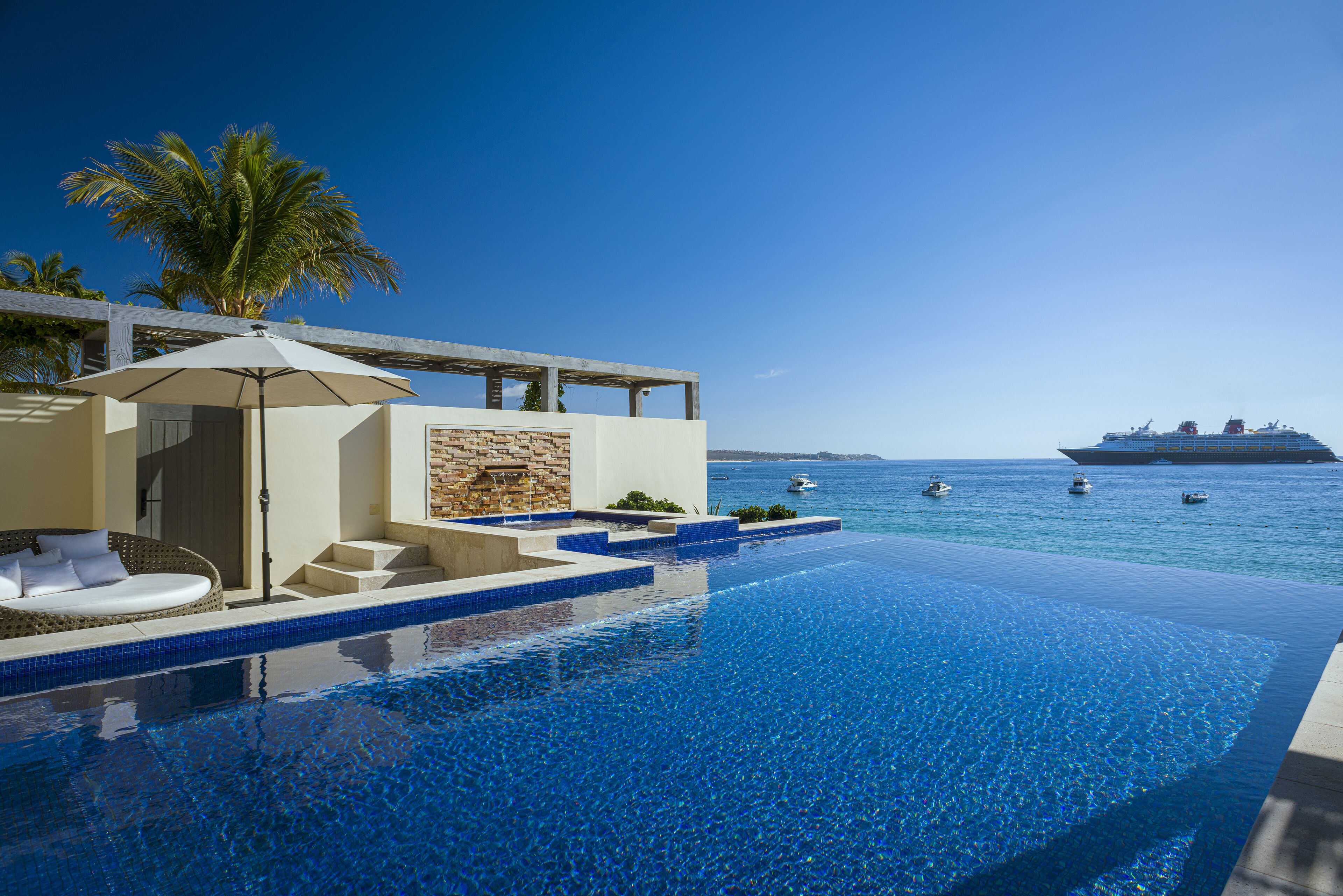 A pool with a clear view of the ocean and a cruise ship in the distance.