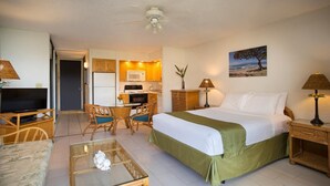 A hotel room with a bed, a TV, a dining table with chairs, a kitchenette, and a painting on the wall.