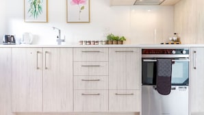 A modern kitchen with light wood cabinets, a stainless steel oven, and a coffee maker on the counter.