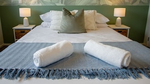 A neatly made bed with white linens, a grey pillow, and two rolled white towels on a blue and white striped blanket.