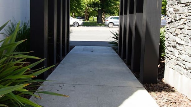 A modern architectural structure with a concrete pathway leading to a parking area.