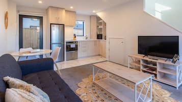A modern living space with a sofa, coffee table, flat-screen TV, and a dining area with a table and chairs.