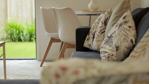 A living room with a sofa, a white chair, and a table with a vase.