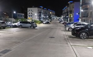 Une vue nocturne d’une rue, avec des voitures garées et des bâtiments.