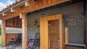 Eine Holzjagdhütte mit Sauna, zwei Lounge-Sesseln und einer kleinen Außen-Sitzgruppe.
