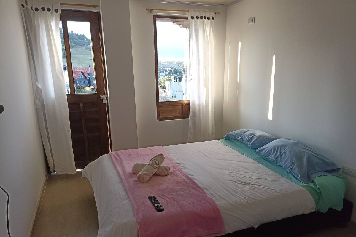 Quarto com cama, janela e vista para uma cidade.