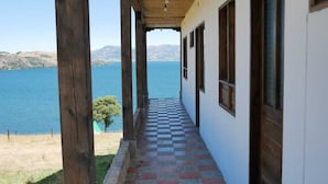 A covered corridor with a checkered floor leading to a building with windows overlooking a body of water. - Hotel Eliseo-Playa Blanca lago de Tota  (Tota)