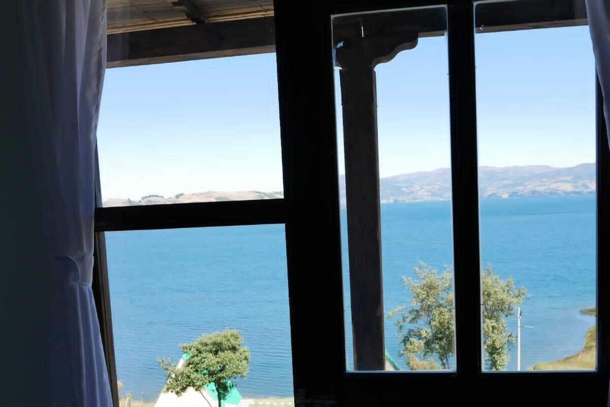 Quarto com grande janela com vista para um corpo d'água e colinas ao longe.
