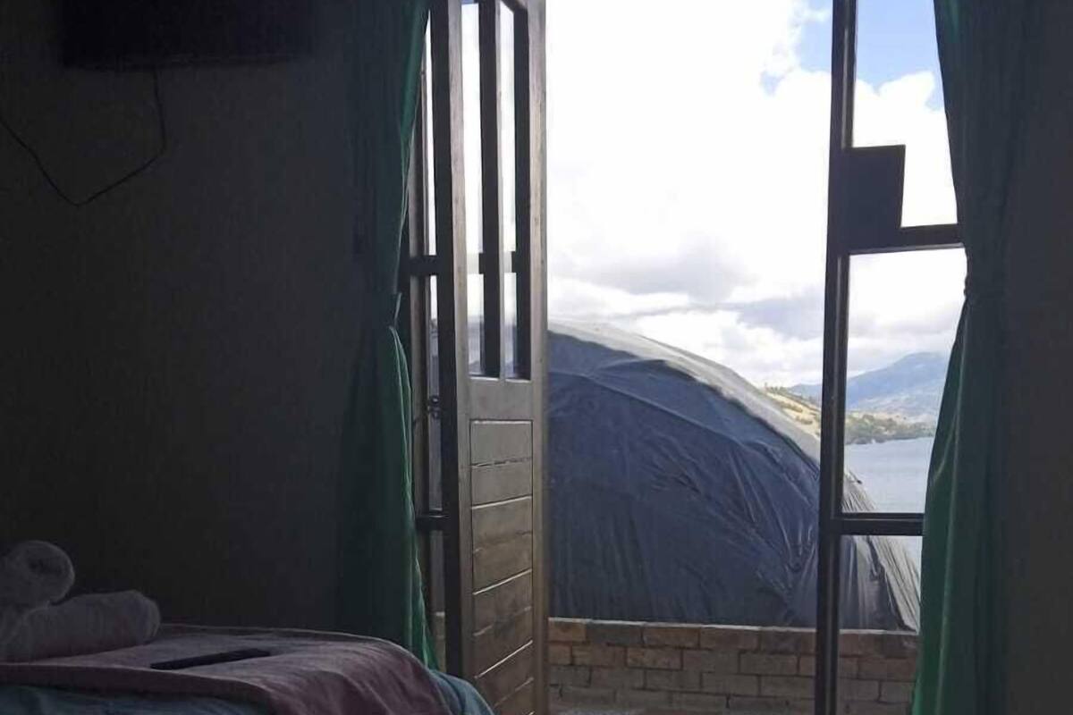 Quarto com cama, porta deslizante para varanda com vista para o mar e montanhas.