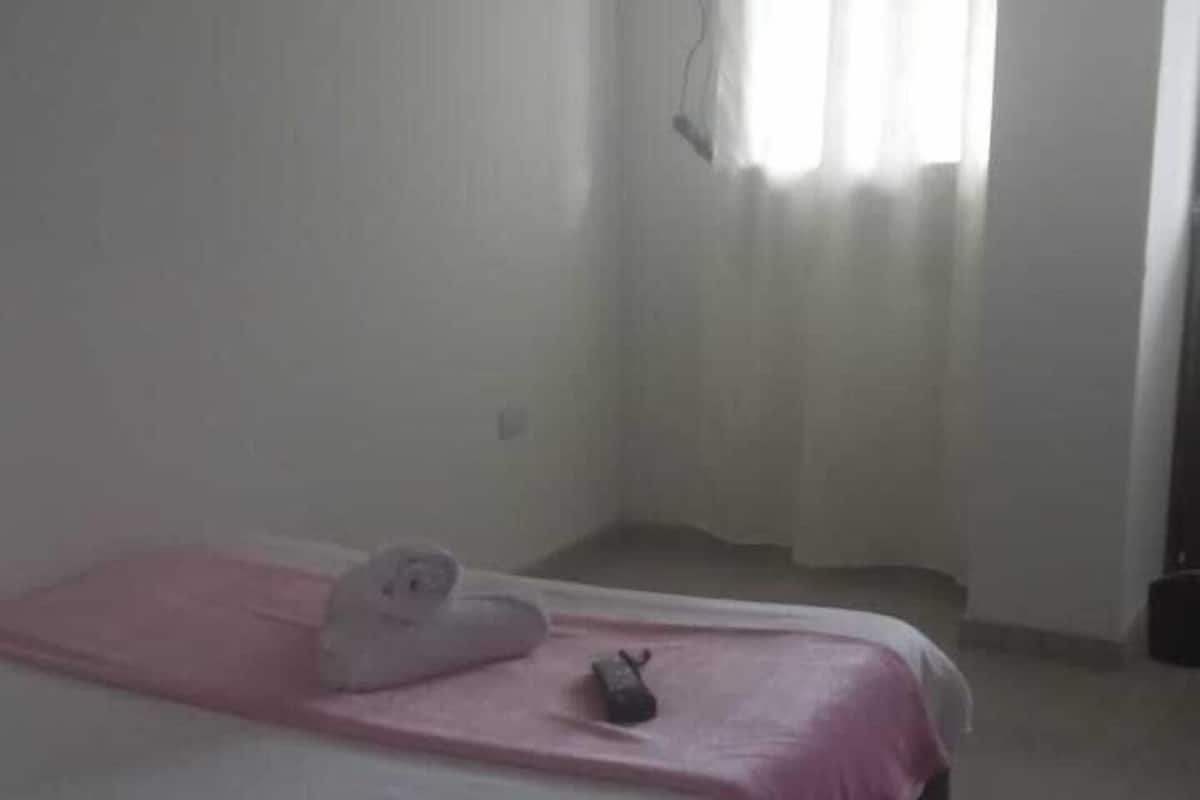 Uma cama de solteiro com um cobertor rosa, uma pequena mesa de cabeceira e uma janela com cortinas.