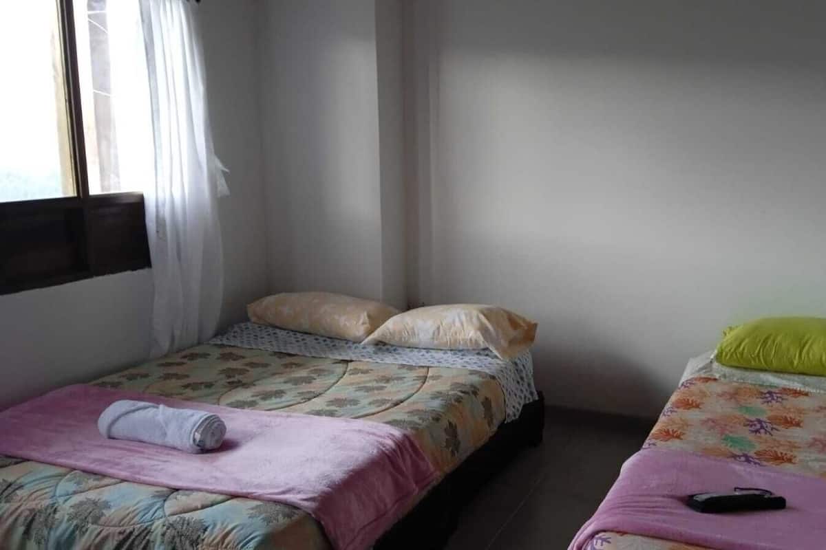 Duas camas de solteiro com roupa de cama floral, um cobertor rosa e um controle remoto na cama da direita.