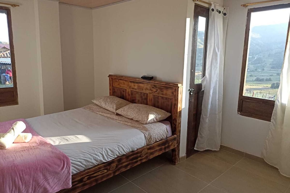 Um quarto com uma cama de madeira, uma janela com vista e uma porta com cortinas.