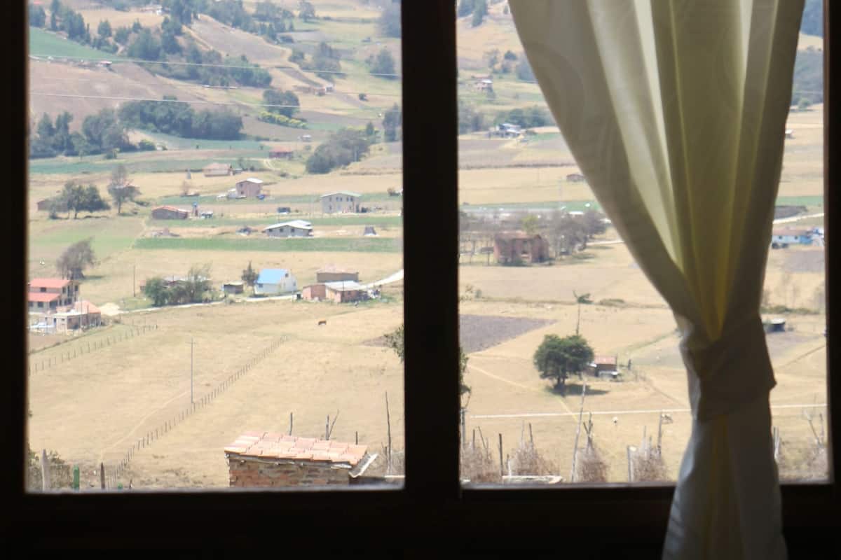 Janela com vista para paisagem rural, incluindo campos, alguns edifícios e colinas ao longe.