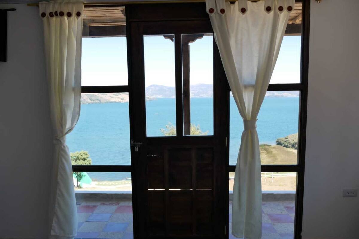 Quarto com uma janela grande com vista para a água e colinas.