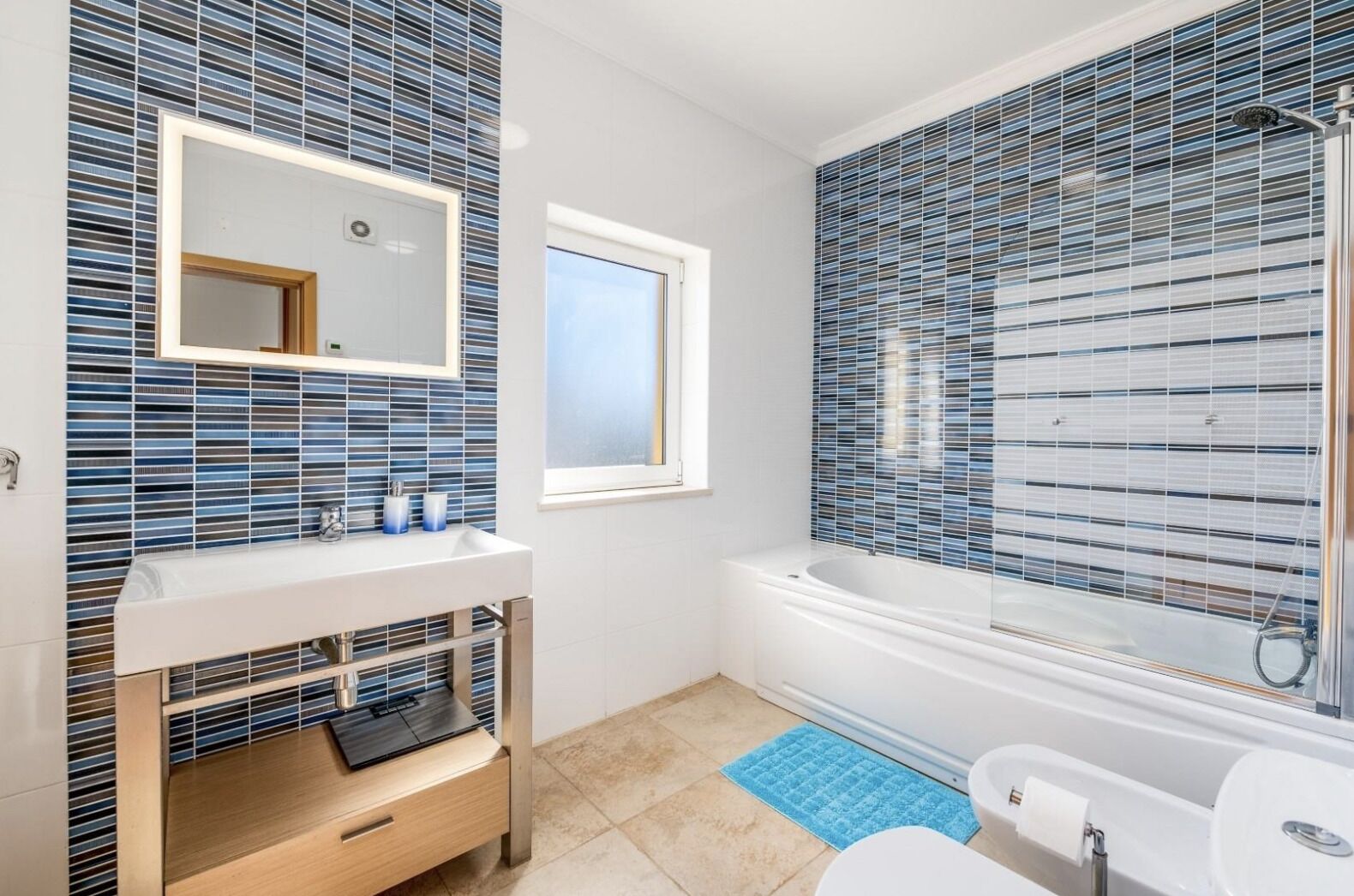 A modern bathroom with a large mirror, a bathtub, and a toilet.