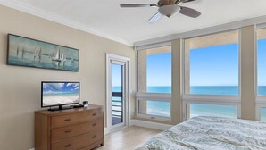 Ein Schlafzimmer mit großem Fenster mit Meerblick, Deckenventilator, Fernseher auf einer Holzkommode und einem Gemälde mit Segelbooten.