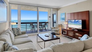 Ein geräumiges Wohnzimmer mit einer großen Couch, einem Couchtisch und einem Fernseher. Das Zimmer verfügt über einen Balkon mit Meerblick.