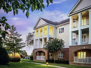 A multi-story residential building with a brick facade, multiple balconies, and a well-maintained lawn.