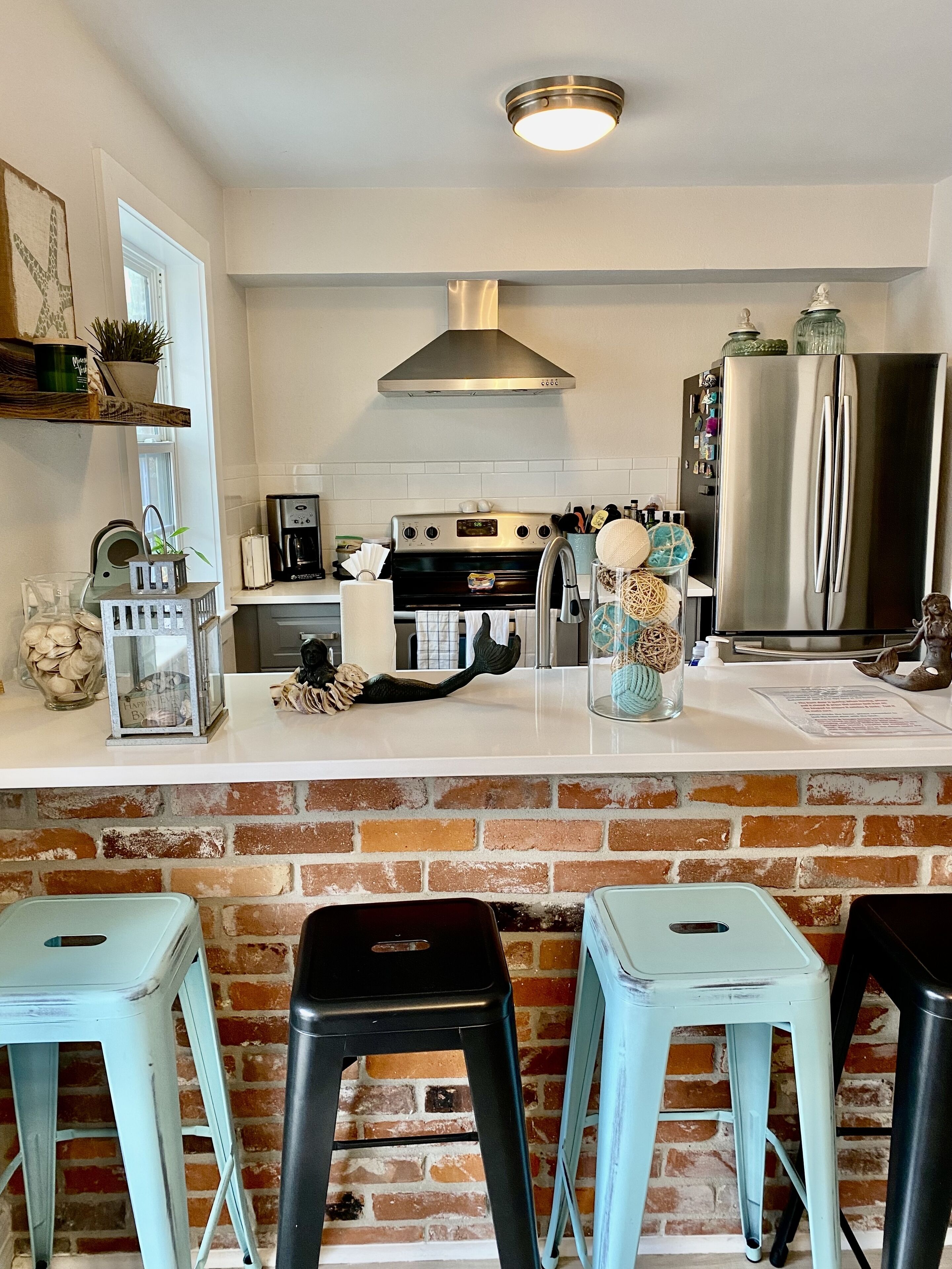 A kitchen with a brick wall, stainless steel appliances, and light blue stools.
