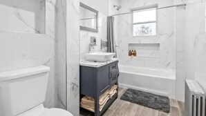 A modern bathroom with a marble wall, a bathtub, a sink, and a toilet.