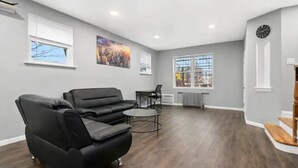 A spacious living room with a black leather sofa, a small round coffee table, and a dining area with a chair and table.