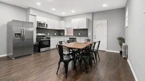 A modern kitchen with white cabinets, stainless steel appliances, and a dining area with a wooden table and black chairs.